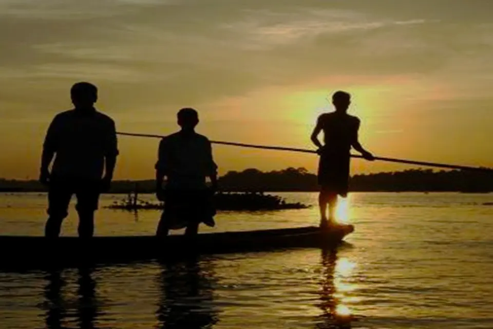 Boatmen poling across a river at sunset