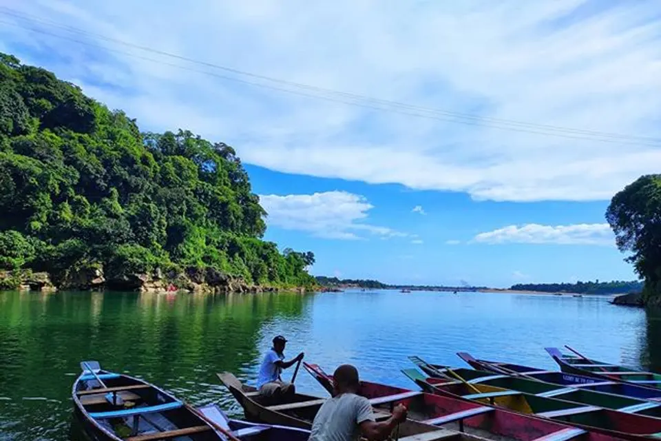 Wooden boats on a clear green river below forested hills