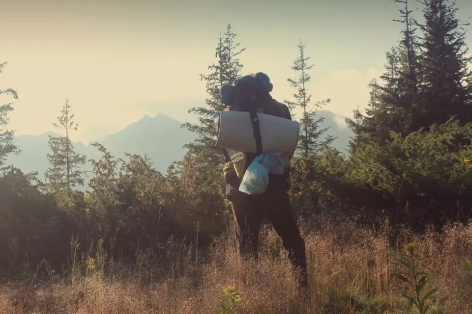 A trekker with a backpack looking out over misty conifer hills