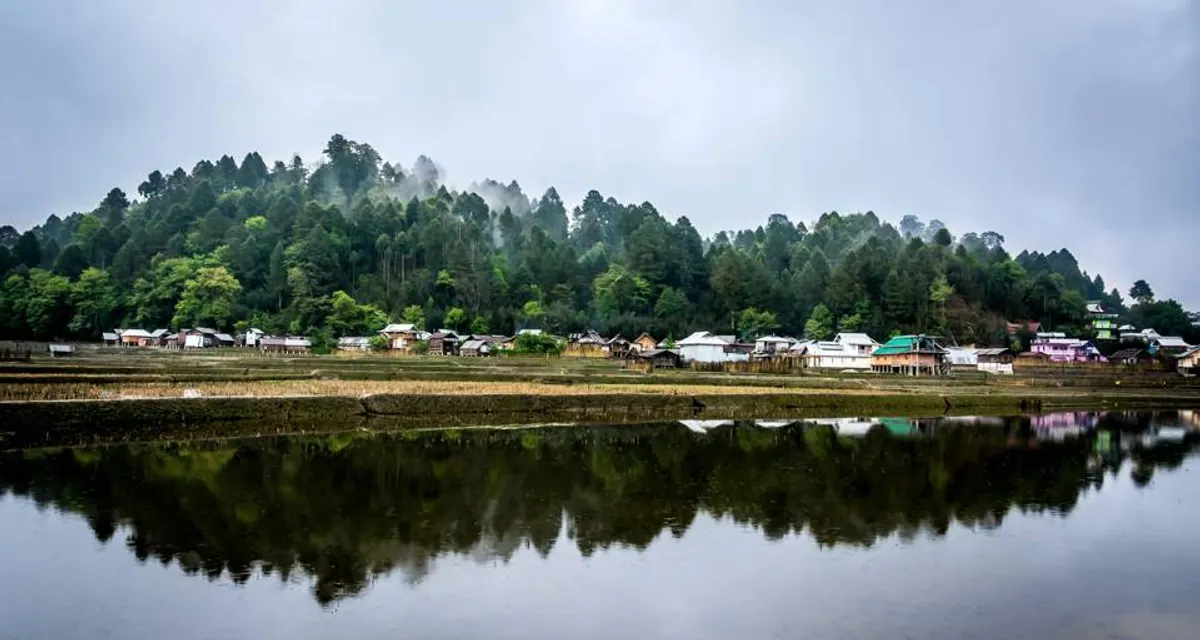 A village beside still water, with forested hills under low cloud